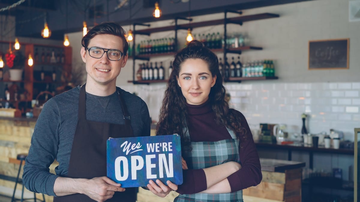 Två caféägare som håller upp en "Open"-skylt i sin verksamhet