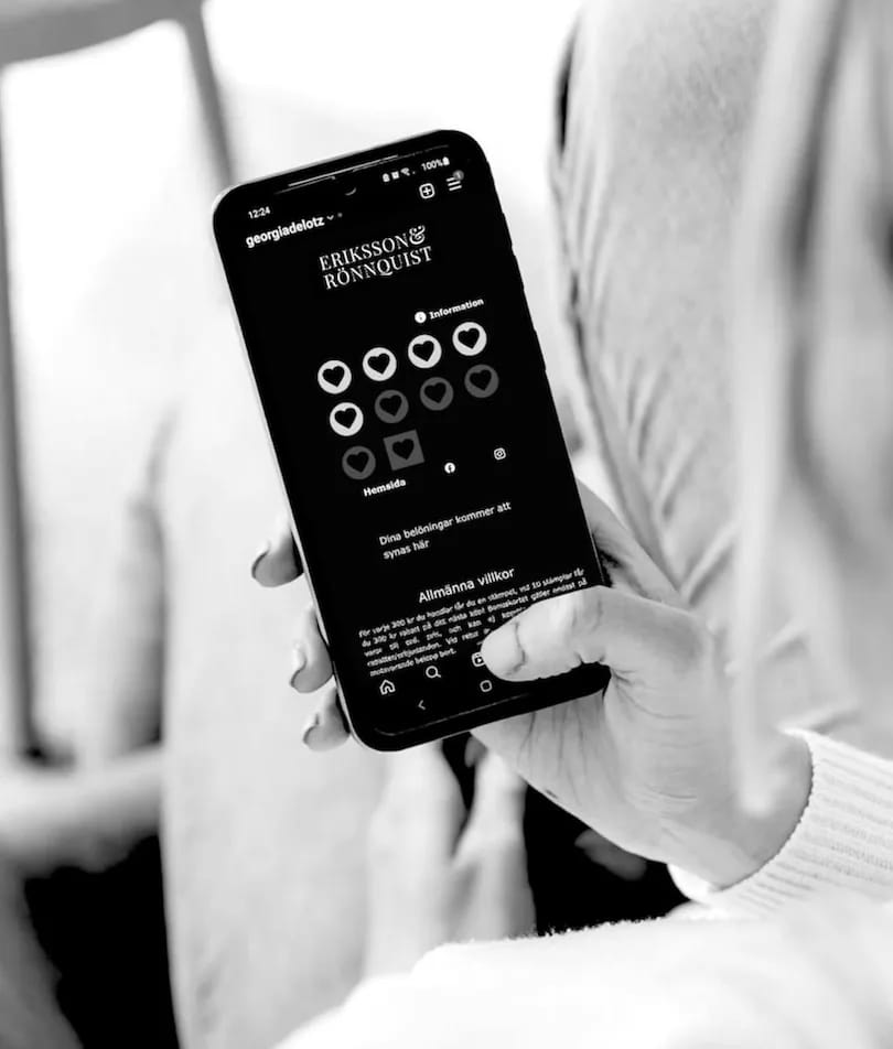 PayAtt GO i kundens hand — svartvitt foto av en hand som håller telefonen med ett brandat stämpelkort öppet